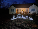 At night, Tina's House features a white silhouette nativity scene that includes Mary, Joseph, and baby Jesus in a manger, along with the three wise men, shepherds, angels, and animals such as a camel and a sheep.